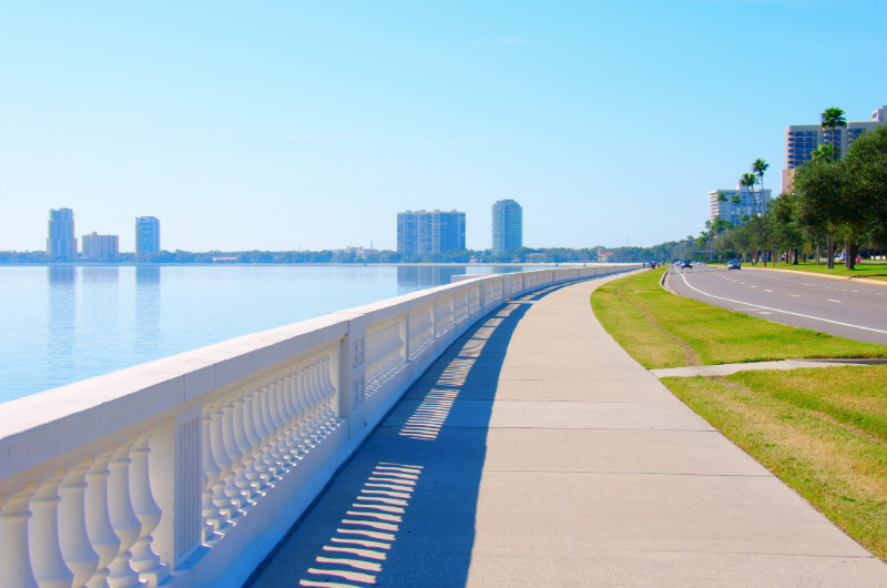 A walkway along the water with buildings in the background.