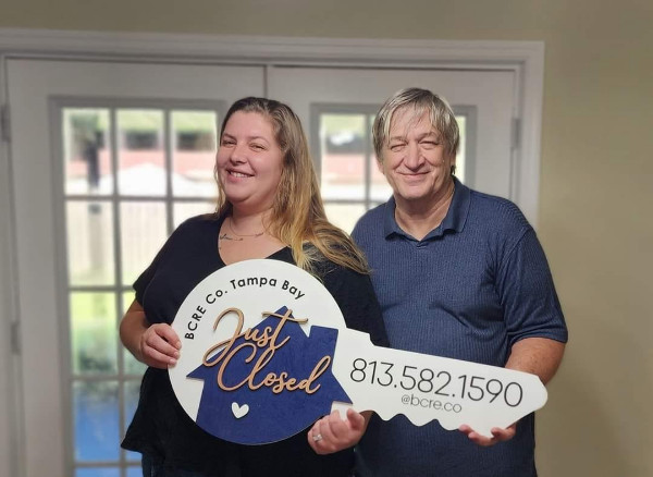 A couple holding up a giant key to their new home.