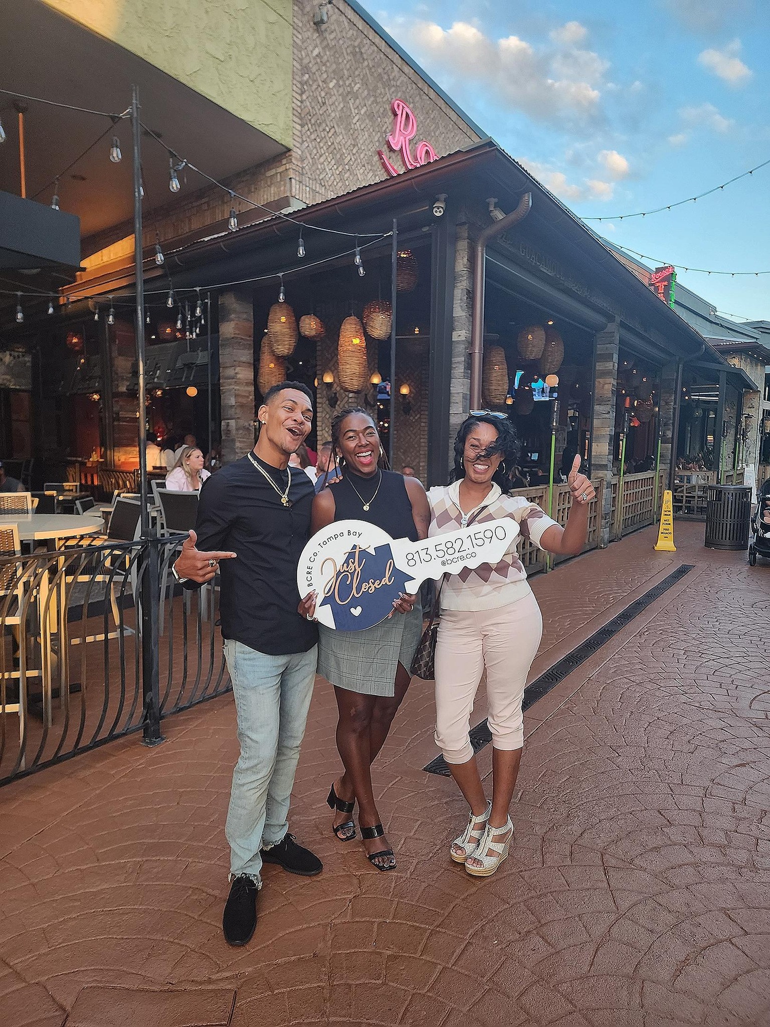 Three people standing on a sidewalk in front of a restaurant.