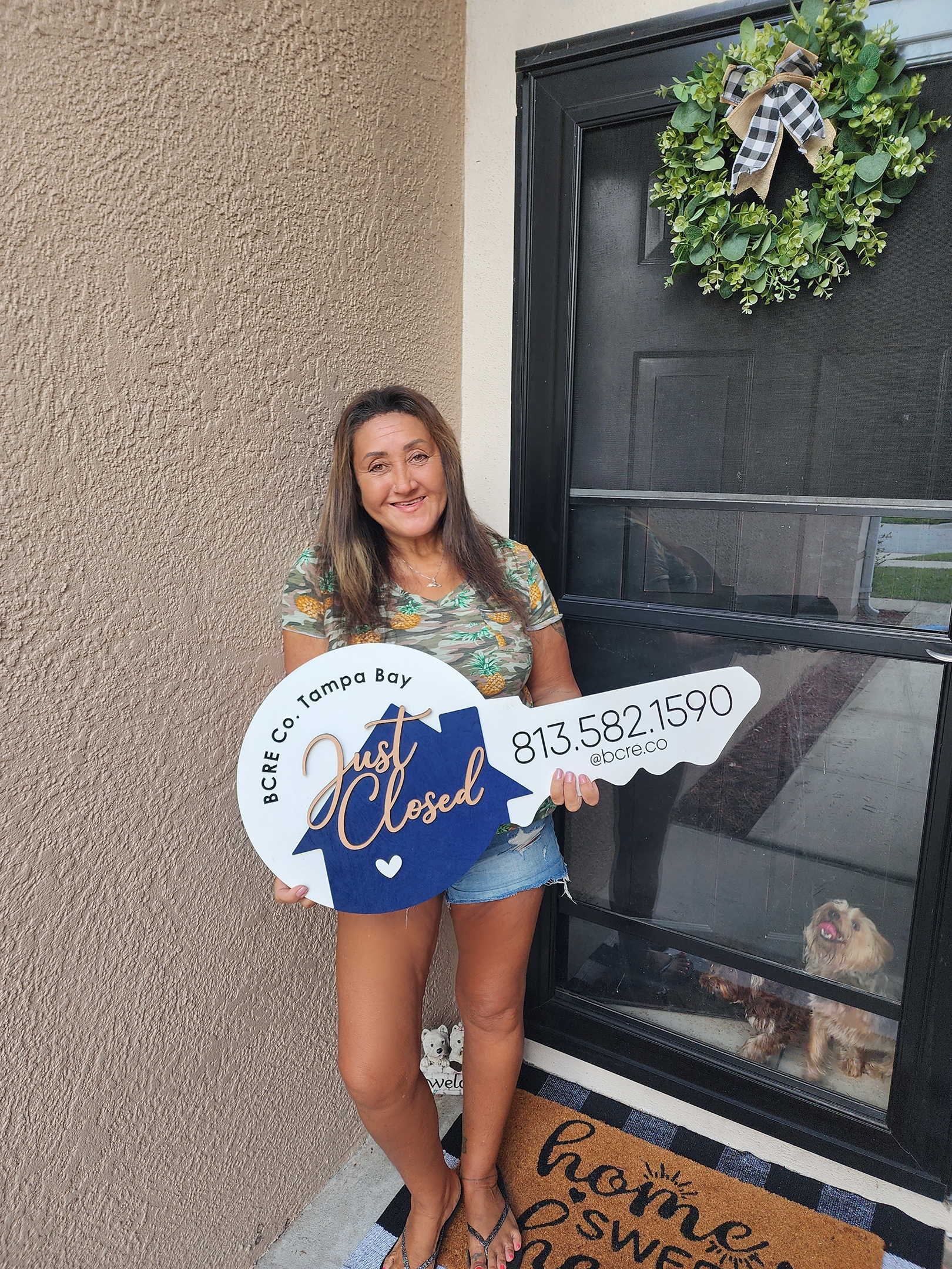 A woman holding a key shaped sign in front of her house.